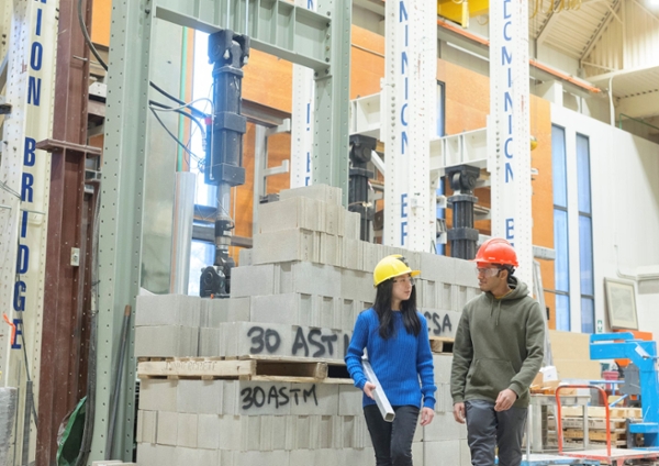 Two students walking in the structures lab wearing hardhats.